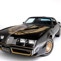 Czarny Pontiac Trans Am z lat 70. z charakterystycznym złotym orłem na masce i złotymi felgami.