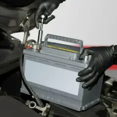 Mechanik w czarnych rękawiczkach wymienia akumulator, co może pomóc w odsiarczanie akumulatora i przywróceniu jego pełnej sprawności.