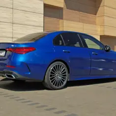 Błękitny Mercedes C 300 z eleganckimi felgami stoi przed nowoczesnym budynkiem.