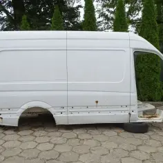 Biała, pusta karoseria Sprinter 906, bez kół i silnika, stoi na betonowej nawierzchni.