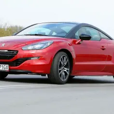 Czerwony Peugeot RCZ z czarnym dachem sunie po drodze, gotowy na zakręty.