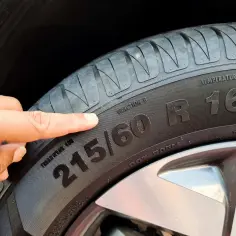 Palec wskazuje na oponę, gdzie widoczny jest rozmiar 215/60 R16. To ważny element, który określa m.in. indeks prędkości opon.