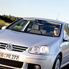 Srebrny Volkswagen Golf z technologią bluemotion jedzie po wiejskiej drodze wśród drzew.