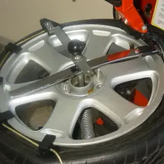 Felga z oponą na maszynie do wulkanizacji. Widać metalowe ramiona i czarne zaciski, które trzymają oponę. To jak kamień milowy w historii motoryzacji, jakby sam Firestone pracował nad tym kołem.