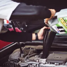 Mechanik wylewa olej silnikowy z butelki Mobil 1 do silnika przez lejek. Szybka wymiana oleju to klucz do długowieczności auta.