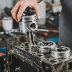 Mechanik montuje tłok do bloku silnika. Widać też inne części silnika.