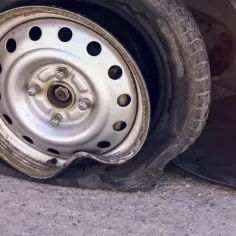 Przebita opona samochodu leży na asfalcie, z felgą wgniecioną i gumą całkowicie spuszczoną.