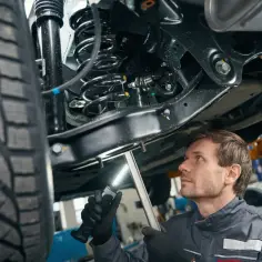 Mechanik bada podwozie auta, oświetlając latarką skomplikowane **zawieszenie** i oponę.