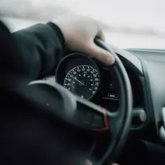 Dłoń na kierownicy, włączony tempomat. Prędkościomierz pokazuje 80 km/h.
