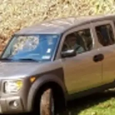Srebrny Honda Element z brązowymi akcentami stoi na trawie, na tle zbocza pokrytego liśćmi.