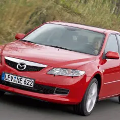 Czerwona Mazda 6 2.0 benzyna w ruchu, za kierownicą uśmiechnięta kobieta.