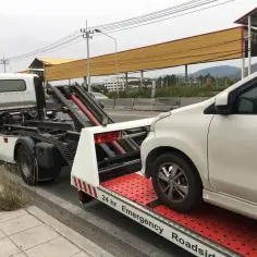 Białe auto jest ładowane na lawetę. Widać, jak holować auto, gdy jest ono umieszczane na platformie.