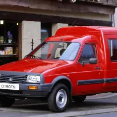 Czerwony Citroen C15, dostawczy klasyk, parkuje przed sklepem z witryną pełną słodkości.