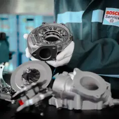 Mechanik w rękawiczkach prezentuje części turbosprężarki, w tym wirnik i obudowę. P0300 - objawy awarii turbiny.