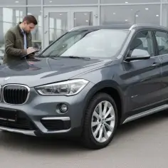 Szary BMW X1 F48 stoi przed salonem, a mężczyzna sprawdza dokumenty.