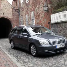 Szary kombi Toyota Avensis T25 na brukowanej uliczce, obok ceglanego budynku z łukiem.