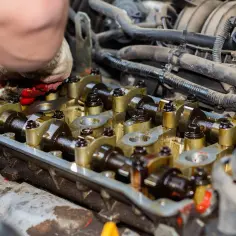 Mechanik w rękawicy pracuje nad zaworami w silniku. Widać wałek rozrządu i elementy układu paliwowego.