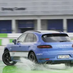 Niebieski Porsche Macan Turbo na mokrym torze Driving Center, rozpryskuje wodę. DSC co to? To system stabilizacji, który pomaga w takich sytuacjach.