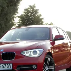 Czerwone BMW 118d na tle drzew i pola.