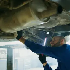 Mechanik bada podwozie Peugeota, szukając przyczyny błędu DTC P0420.