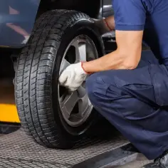 Mechanik w białych rękawiczkach dokręca śruby koła. Czas pomyśleć, kiedy wymienić opony na letnie.
