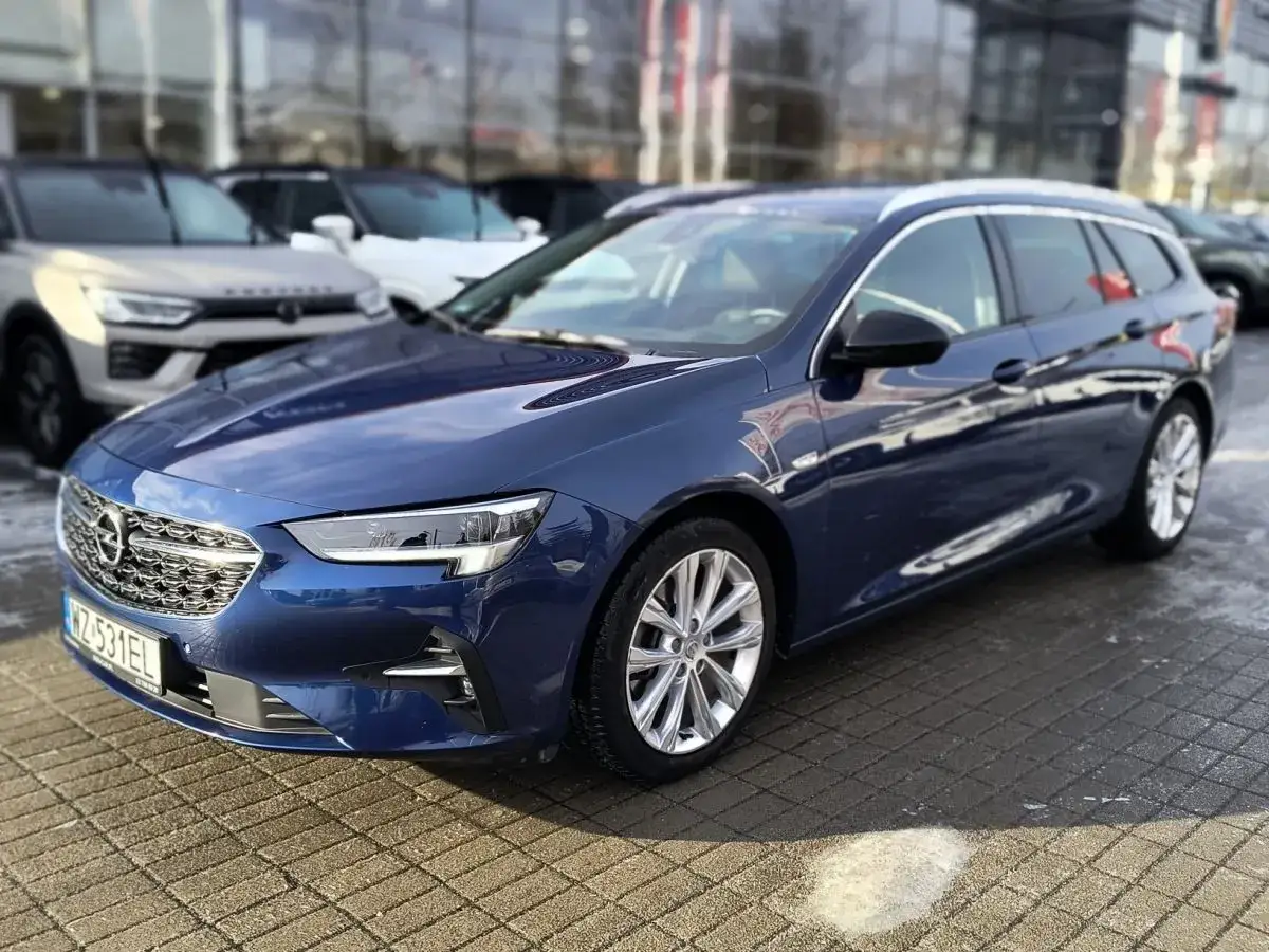 Błękitny Opel Insignia 2.0 Turbo kombi na parkingu przed salonem samochodowym.