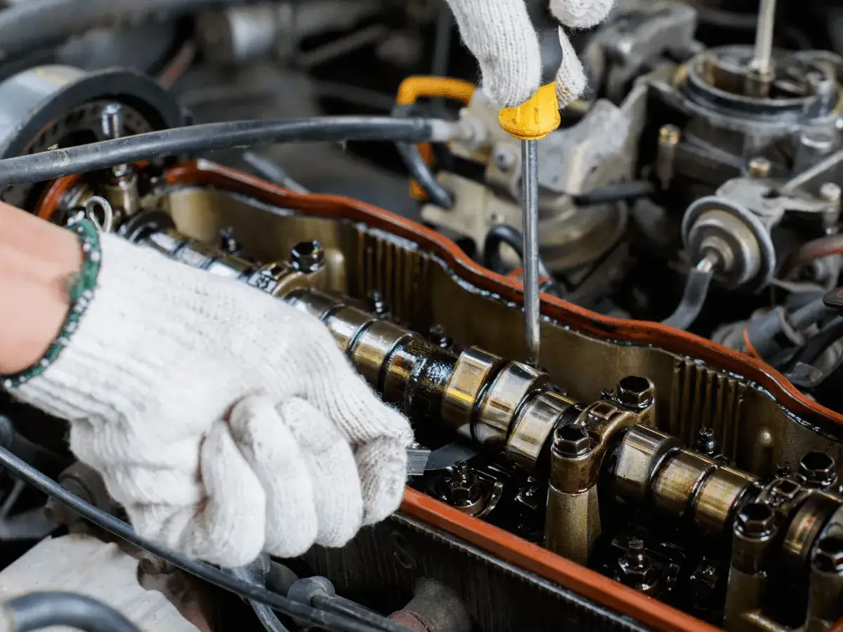 Mechanik reguluje luzy zaworowe w silniku, używając śrubokręta.
