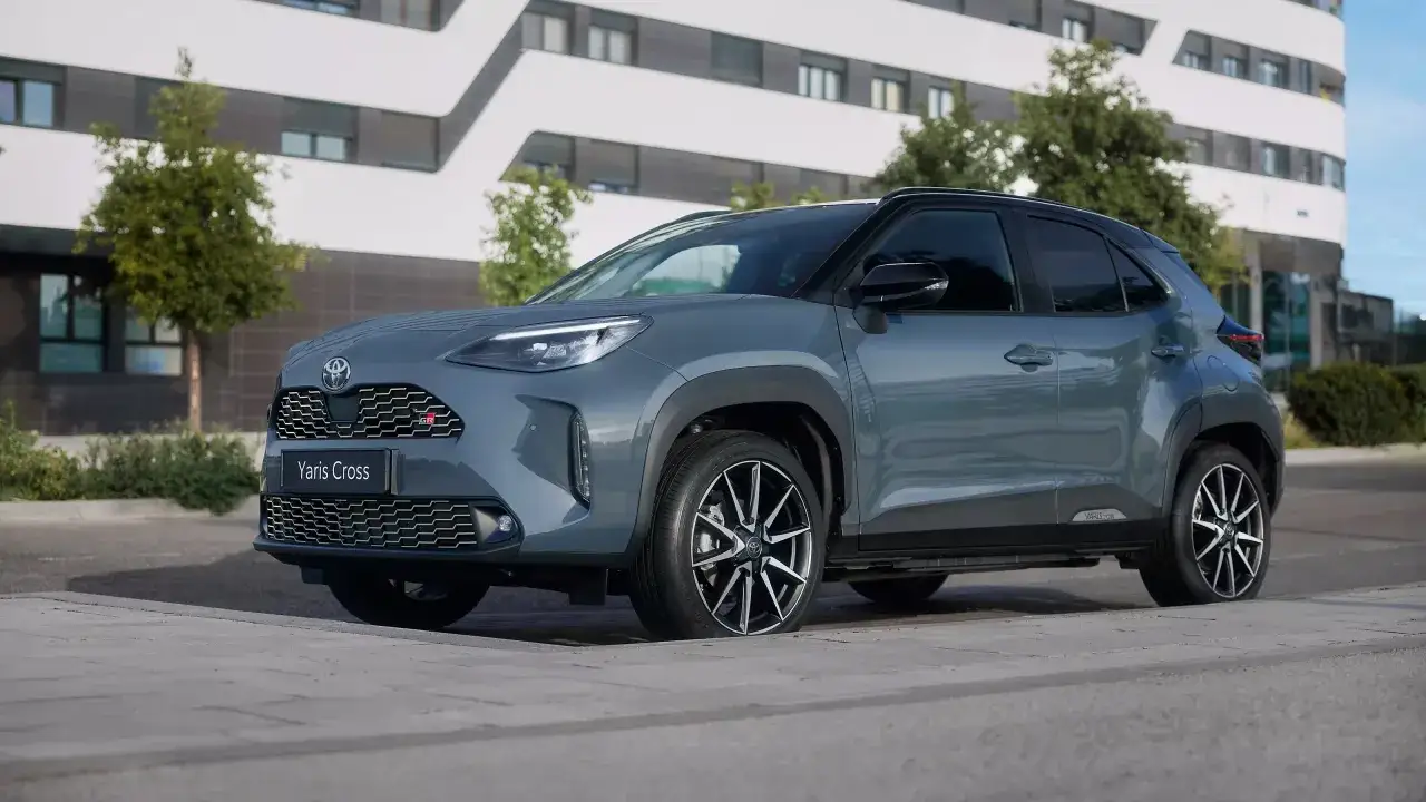 Szary Toyota Yaris Cross GR Sport, stylowy SUV hybrydowy, zaparkowany przed nowoczesnym budynkiem.