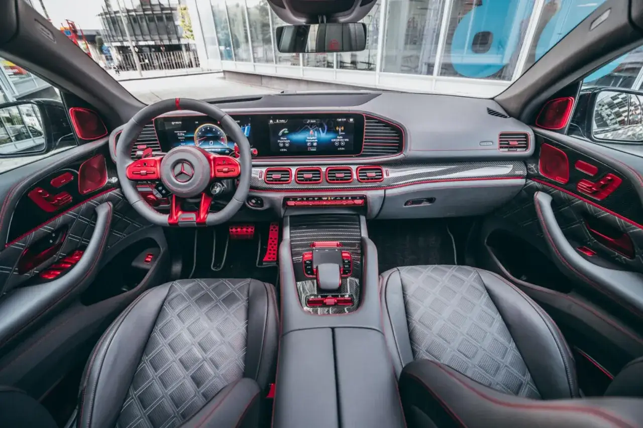 Wnętrze luksusowego SUV-a z czerwonymi akcentami i pikowanymi fotelami. Widać kierownicę, deskę rozdzielczą z ekranami i konsolę środkową. To przykład udanych retrofitów.