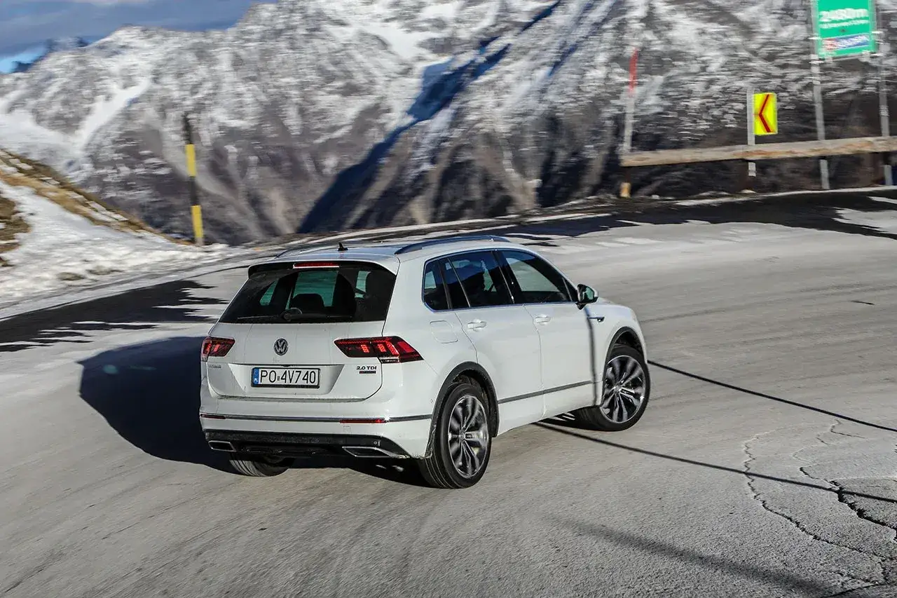 Biały Volkswagen Tiguan z napędem 4motion pokonuje górską, krętą drogę. W tle ośnieżone szczyty.