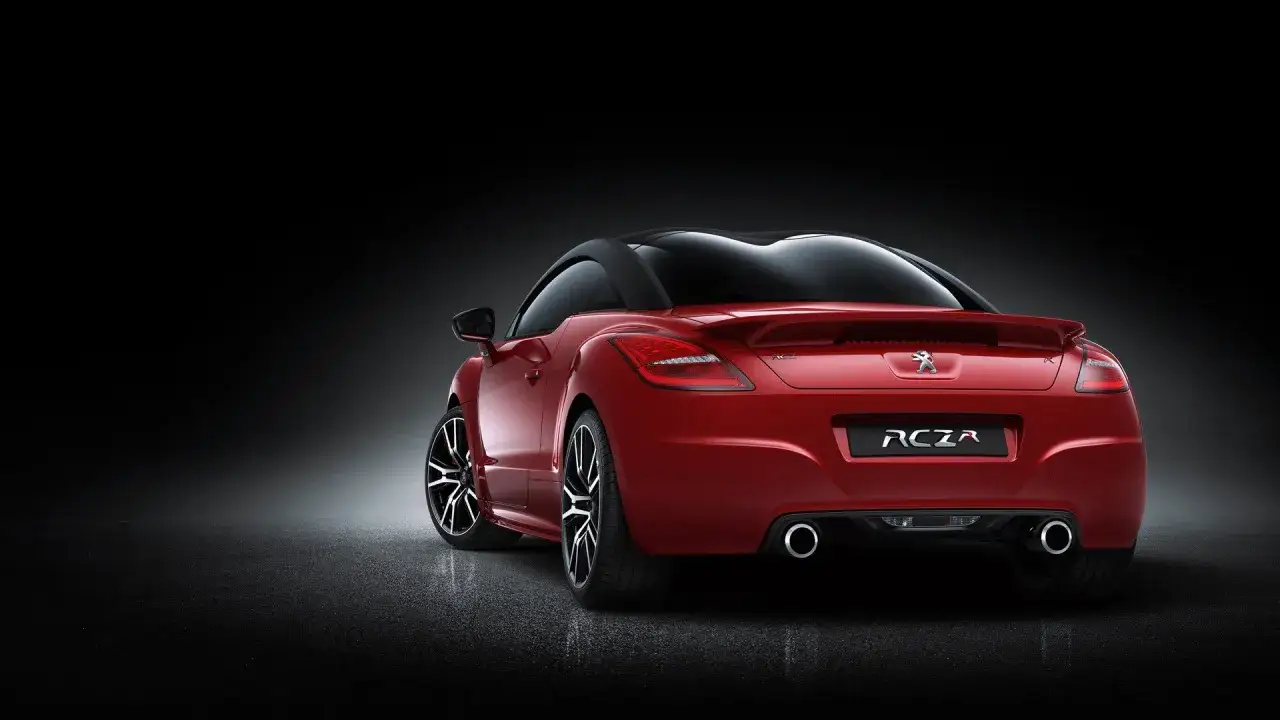 Czerwony Peugeot RCZ z czarnym dachem, prezentujący swoje sportowe linie i felgi na ciemnym tle.