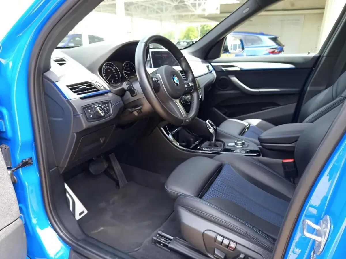 Wnętrze niebieskiego BMW X1 F48 z czarną tapicerką i niebieskimi akcentami. Widok na deskę rozdzielczą, kierownicę i fotele.