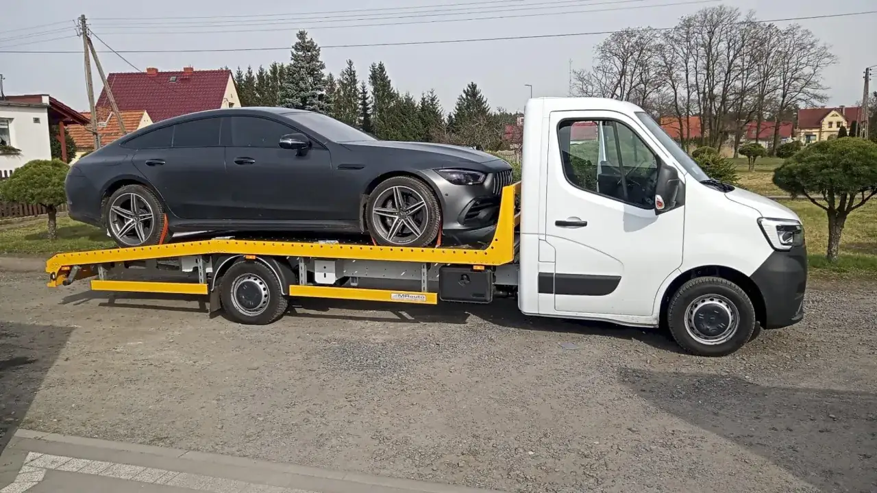 Ciemnoszary sportowy samochód na żółtej lawecie. Pokazano, jak holować auto, gdy jest unieruchomione.