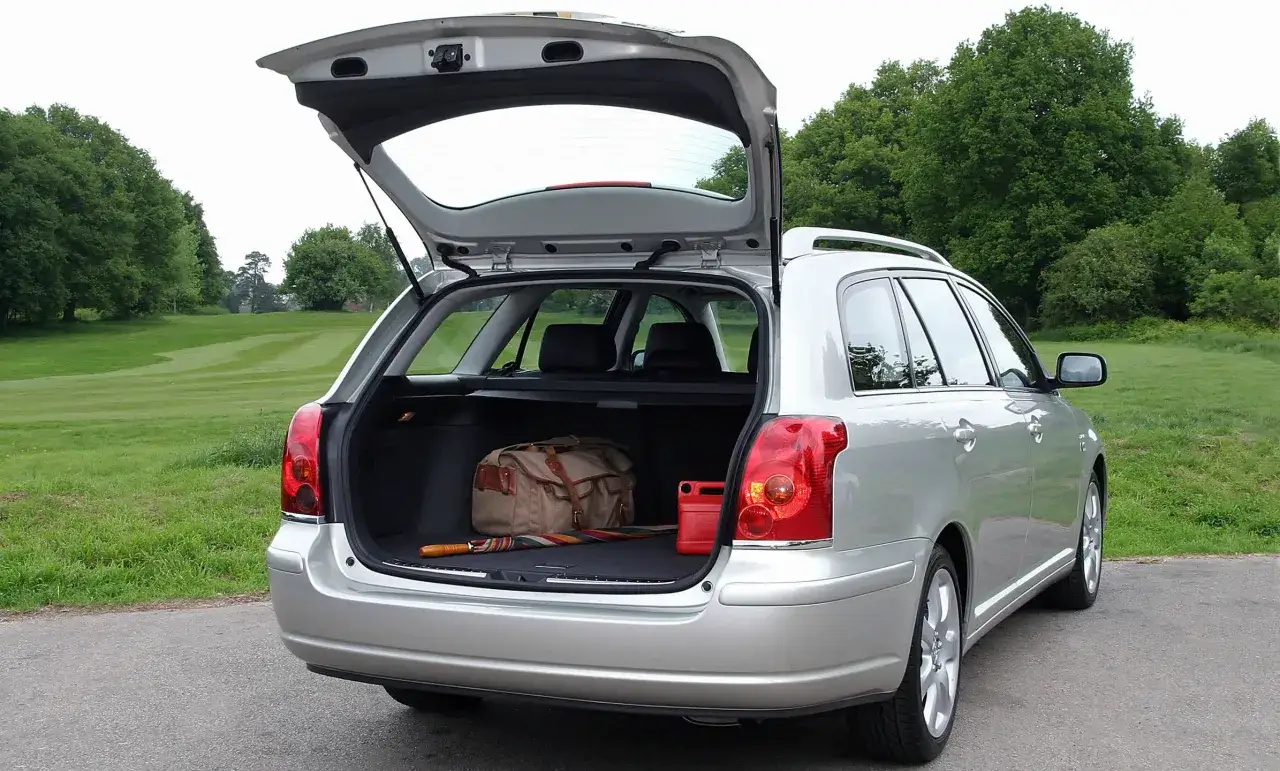 Srebrny Toyota Avensis T25 2.0 D4D z otwartym bagażnikiem, w którym znajduje się torba podróżna, parasol i czerwony kanister.