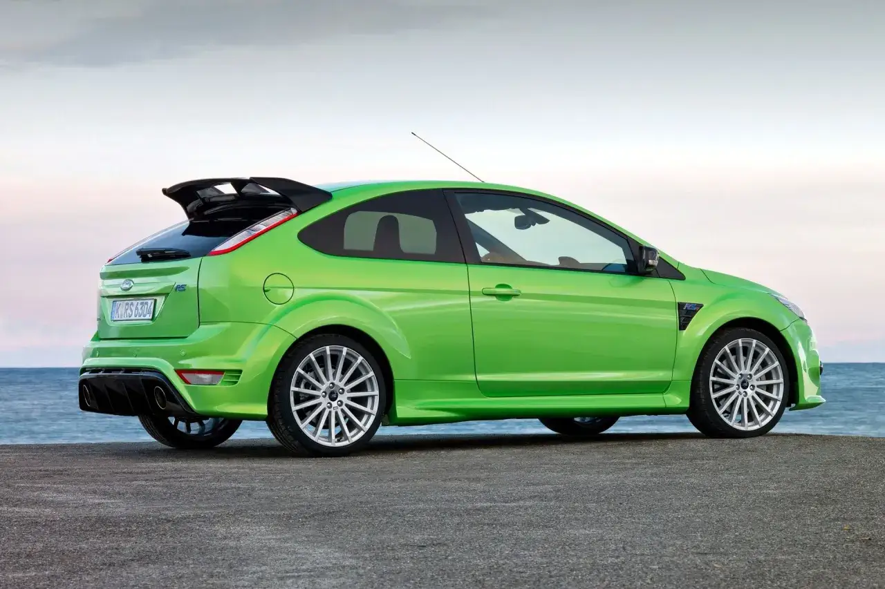 Zielony Ford Focus RS MK2 z charakterystycznym spojlerem i dyfuzorem, zaparkowany nad morzem.