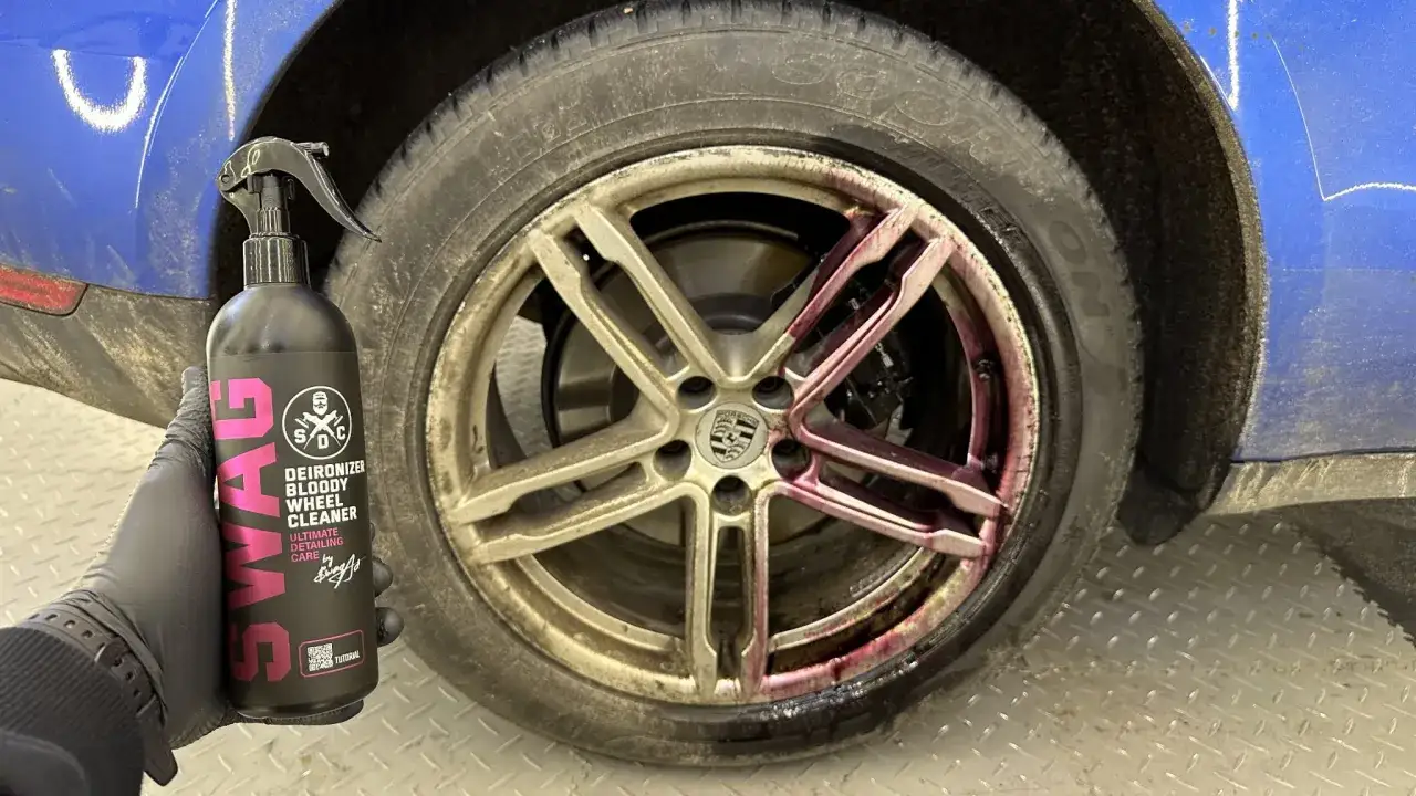 Rękawica w czarnej rękawiczce trzyma butelkę z preparatem do czyszczenia felg. Na brudnej, srebrnej feldze Porsche widać fioletowy płyn, który reaguje z zanieczyszczeniami.