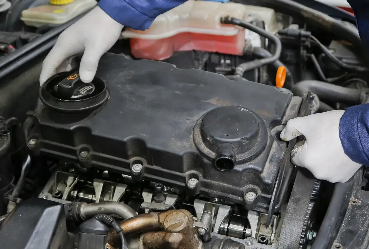 Mechanik w białych rękawiczkach sprawdza silnik, odkręca korek wlewu oleju i kontroluje stan paska rozrządu.