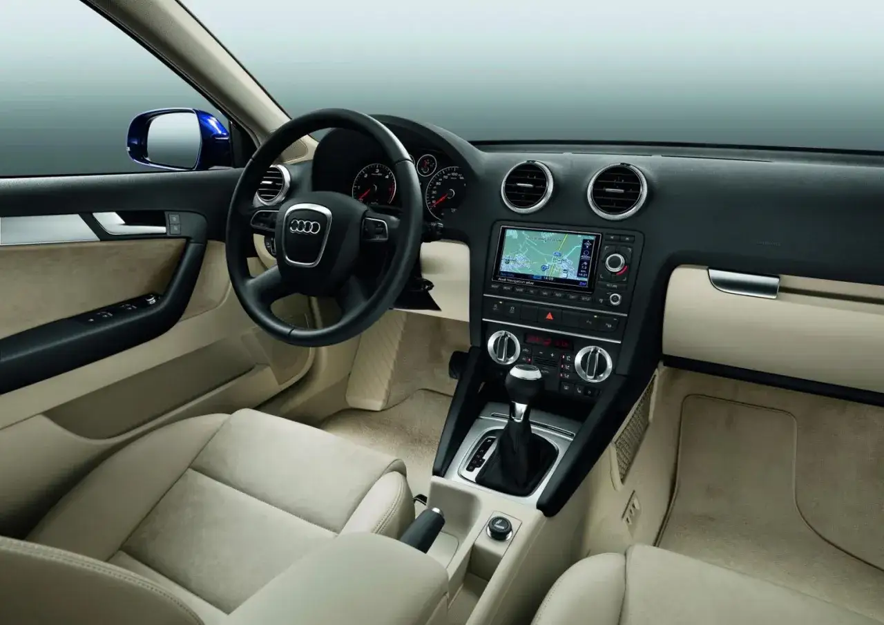 Wnętrze Audi A3 2004 z jasną tapicerką, nawigacją i manualną skrzynią biegów.
