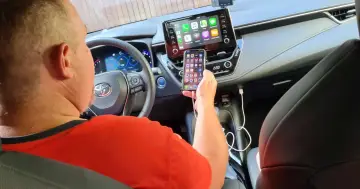 Mężczyzna podłącza iPhone'a do systemu multimedialnego samochodu, pokazując, jak nowoczesne retrofity ułatwiają życie.